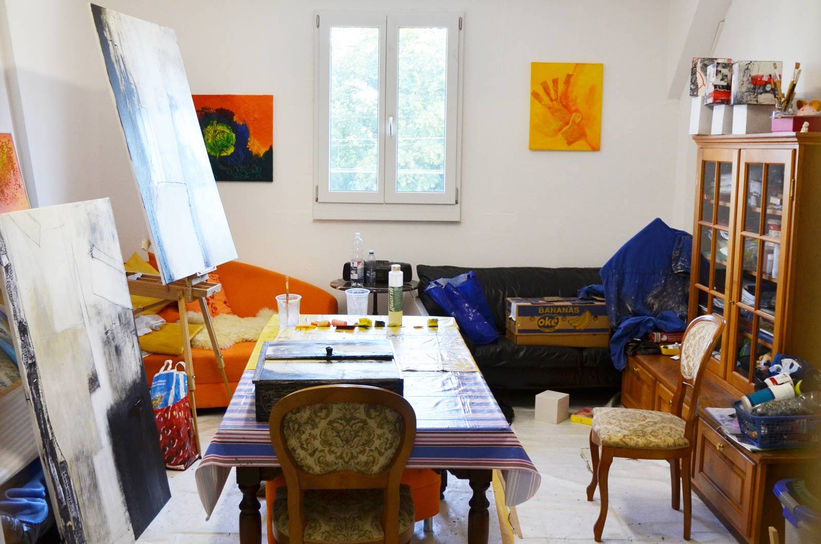 Ein farbenfrohes Malatelier mit Leinwänden, Farben und Kunstwerken an den Wänden.