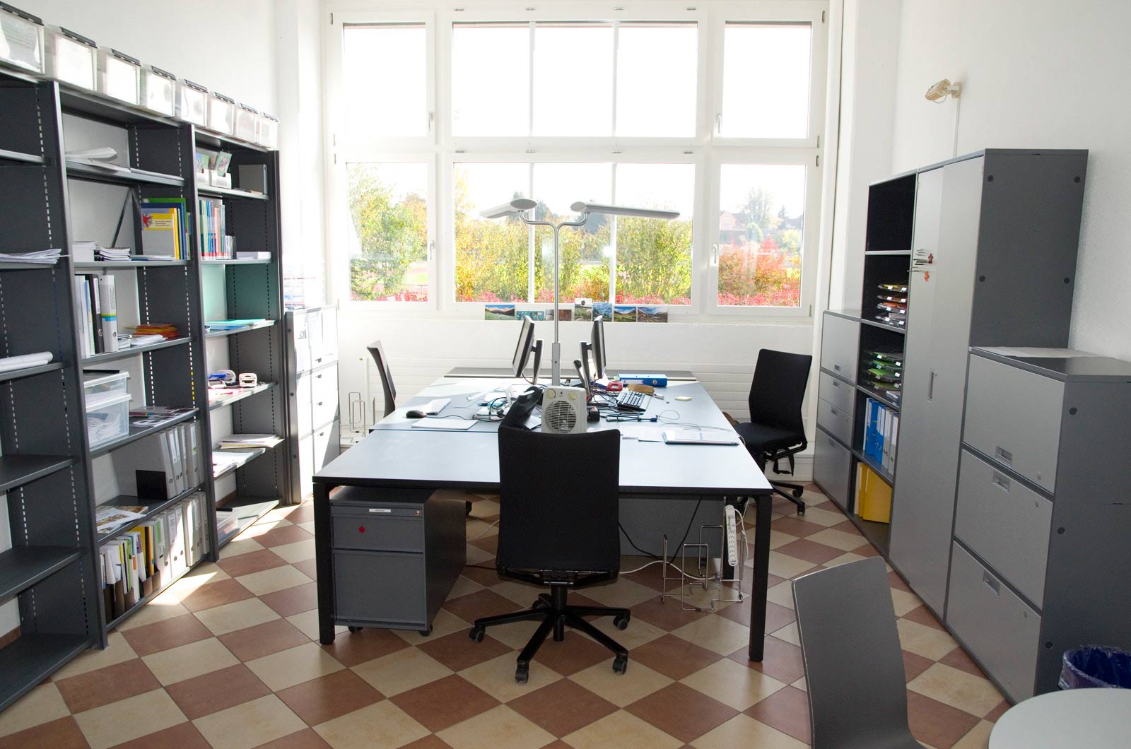Ein helles, modernes Büro mit Schreibtisch und Blick auf Bäume durch große Fenster.