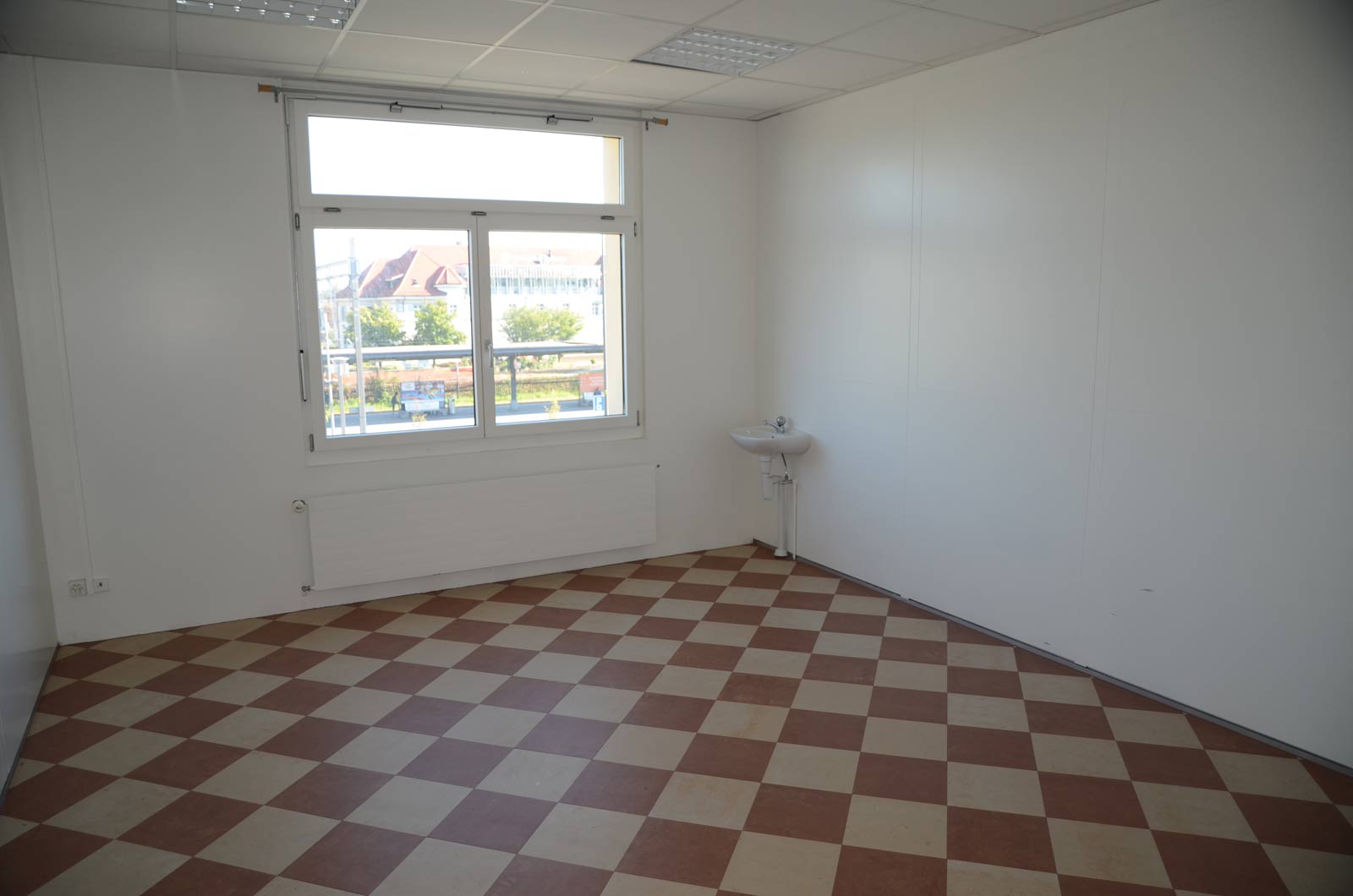 Ein leerer, heller Büroraum mit Schachbrettboden und einer Wandspüle.