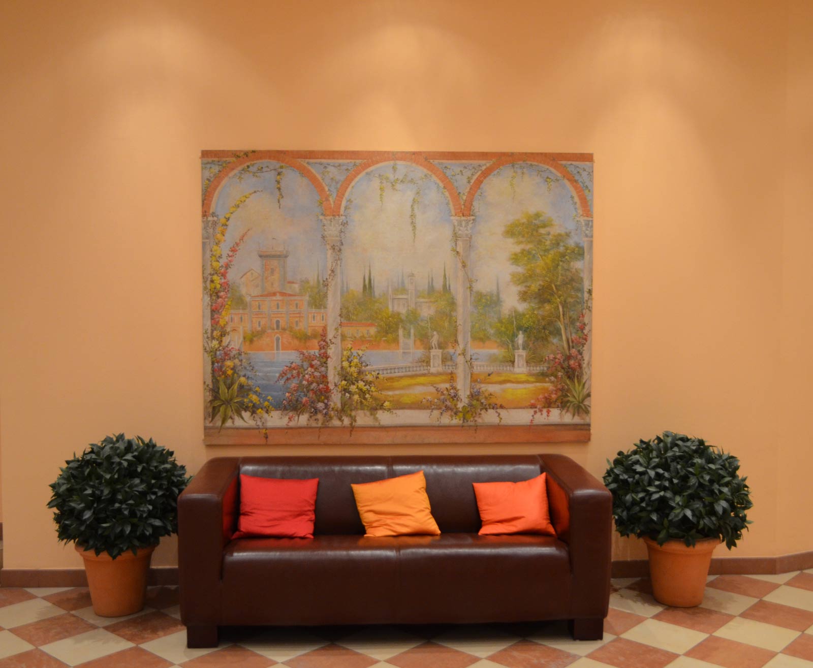 Ein einladender Empfangsraum mit dunklem Sofa, Wandgemälde und Pflanzen in warmen Farben.