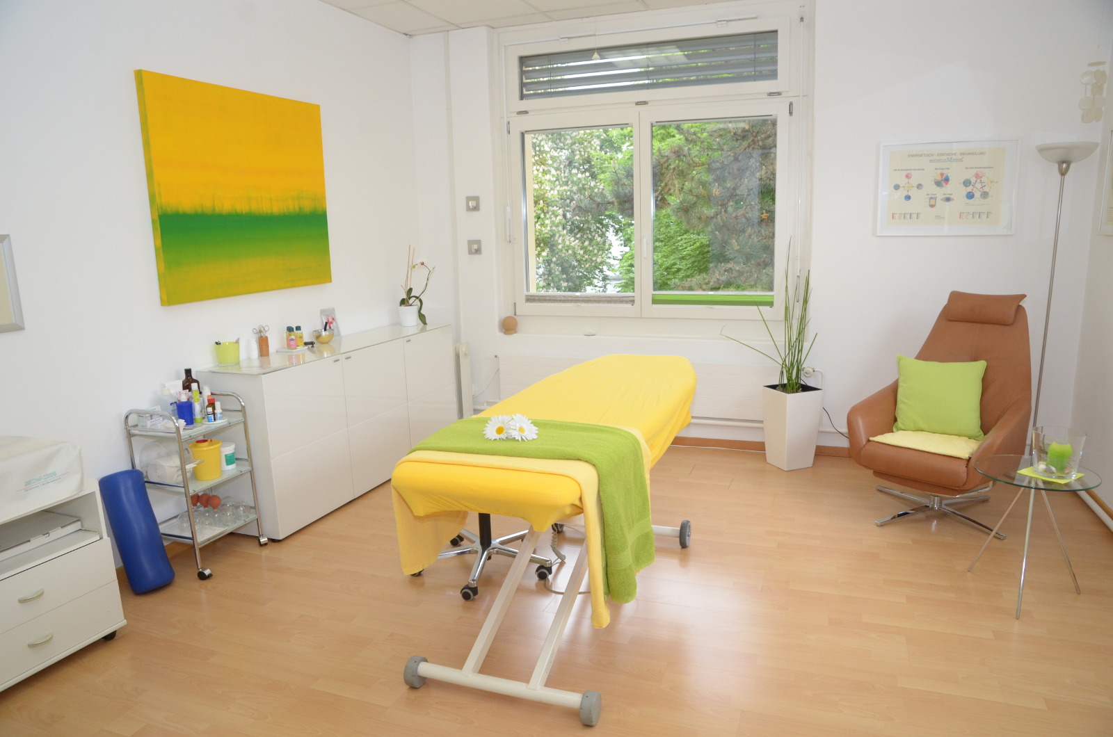 Ein heller Raum mit einem gelb-grün gedeckten Liegebett, Pflanzen und Wandkunst.