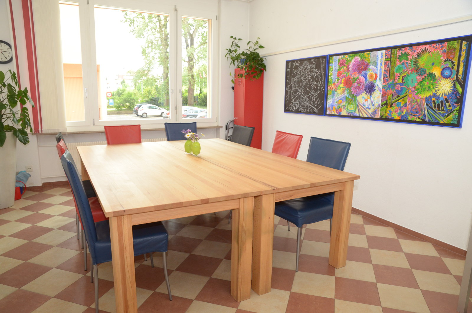 Ein heller Raum mit einem großen Holztisch, bunten Stühlen und Wandkunst.